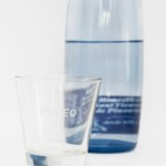 Das Pineo Wasserglas mit der Flasche im Hintergrund.