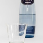 Pineo Glasflasche mit Glas im Vordergrund. Natürliches, selbst entspringendes Mineralwasser aus den spanischen Pyrenäen.